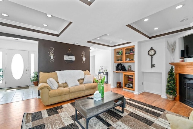 living room with light wood-type flooring, a tray ceiling, and ornamental molding