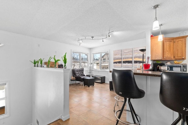 kitchen featuring a textured ceiling, kitchen peninsula, a breakfast bar area, and hanging light fixtures