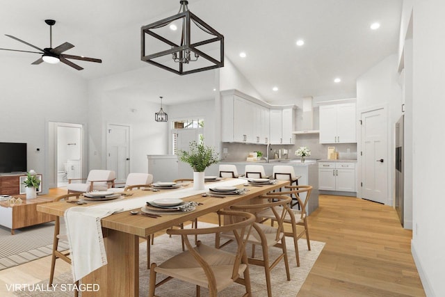 dining room featuring ceiling fan with notable chandelier, light hardwood / wood-style floors, high vaulted ceiling, and sink