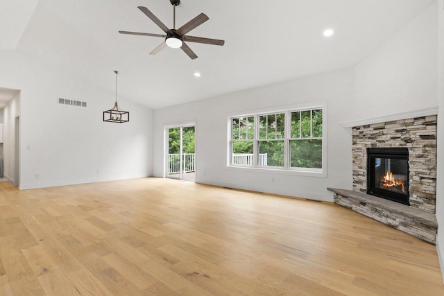 unfurnished living room with ceiling fan, a stone fireplace, light wood-type flooring, and vaulted ceiling