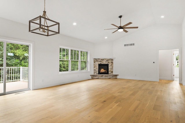 unfurnished living room featuring a stone fireplace, high vaulted ceiling, ceiling fan with notable chandelier, and light wood-type flooring