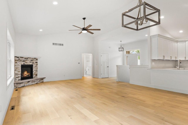 unfurnished living room with high vaulted ceiling, sink, ceiling fan, a fireplace, and light hardwood / wood-style floors