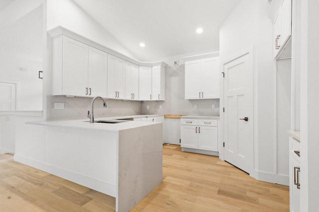 kitchen with white cabinets, sink, vaulted ceiling, light hardwood / wood-style floors, and kitchen peninsula