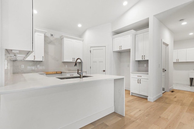 kitchen featuring white cabinetry, sink, light hardwood / wood-style flooring, backsplash, and kitchen peninsula