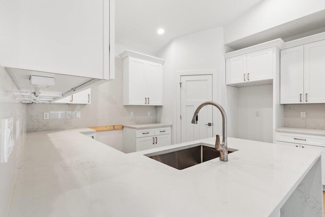 kitchen with backsplash, kitchen peninsula, white cabinetry, and sink