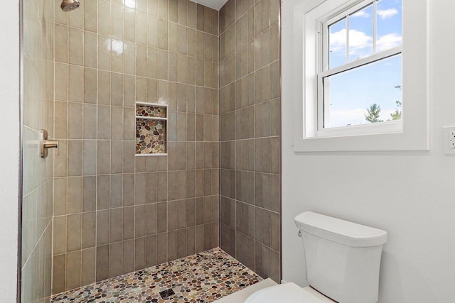 bathroom featuring toilet, a tile shower, and a wealth of natural light