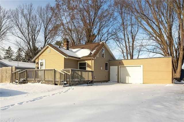 snow covered back of property featuring a garage and a wooden deck