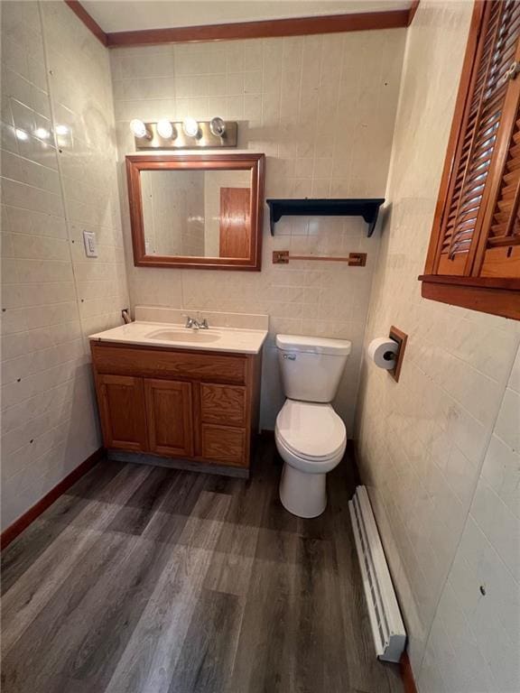 bathroom with a baseboard heating unit, hardwood / wood-style floors, toilet, vanity, and tile walls