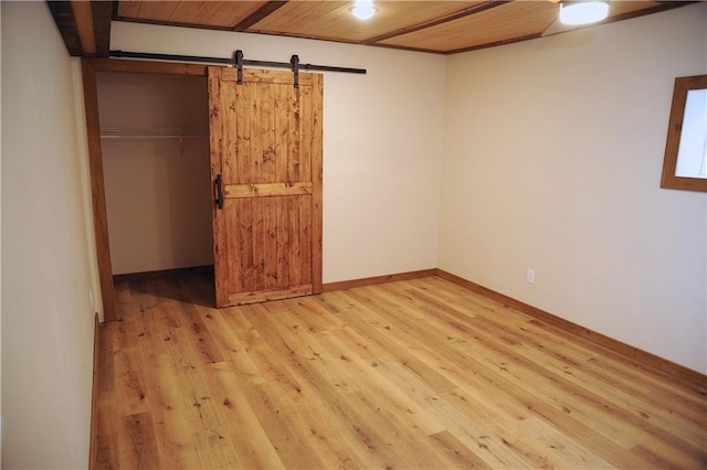 unfurnished bedroom with a barn door, a closet, wooden ceiling, and light hardwood / wood-style flooring