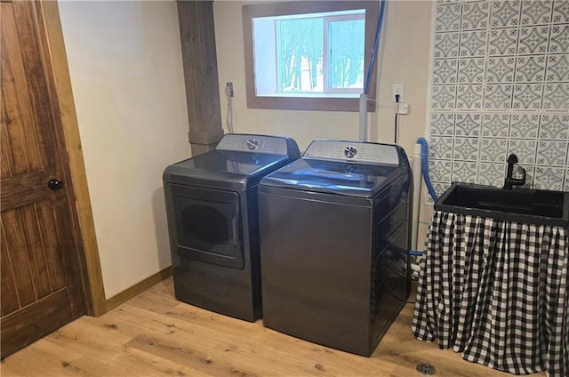 clothes washing area with washer and clothes dryer, light hardwood / wood-style floors, and sink