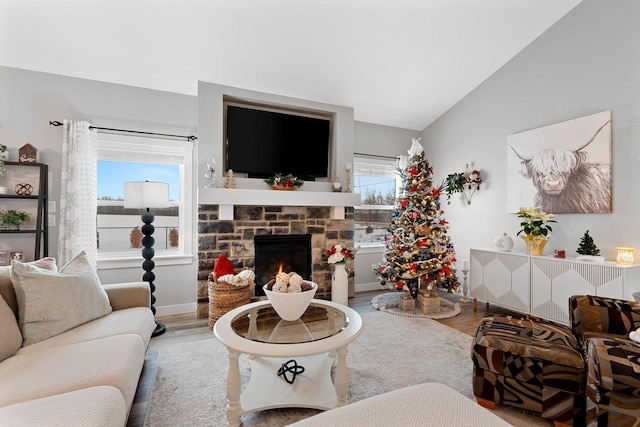 living room featuring plenty of natural light, a stone fireplace, lofted ceiling, and wood-type flooring