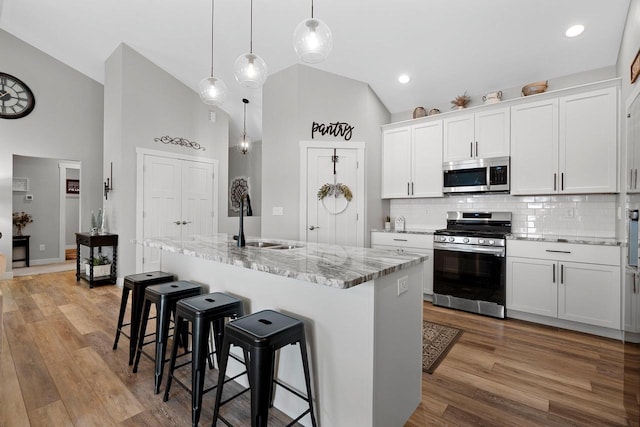 kitchen featuring backsplash, stainless steel appliances, sink, white cabinets, and an island with sink