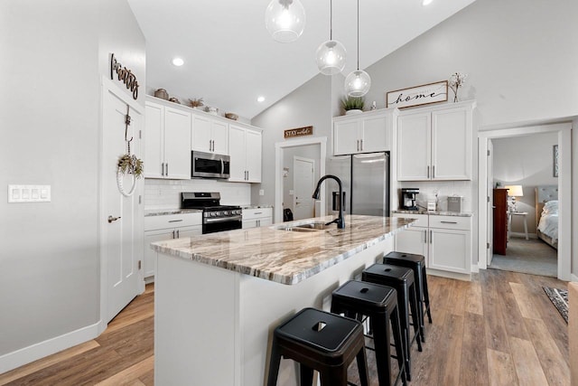 kitchen featuring white cabinetry, sink, stainless steel appliances, backsplash, and a center island with sink