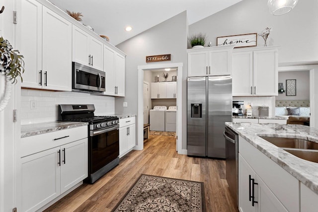 kitchen with lofted ceiling, white cabinetry, separate washer and dryer, and stainless steel appliances