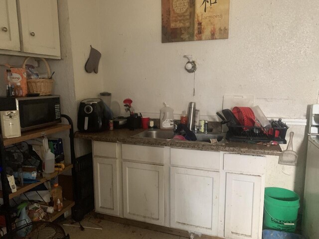 kitchen with white cabinetry, dark countertops, black microwave, and a sink