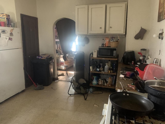 kitchen with freestanding refrigerator, arched walkways, white cabinets, black microwave, and light floors