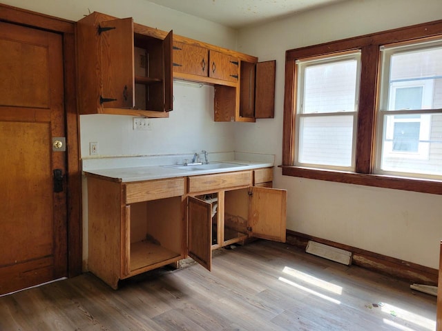 kitchen with open shelves, brown cabinets, a sink, light countertops, and light wood-style flooring