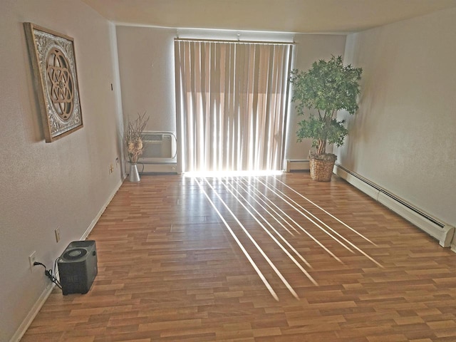 unfurnished room featuring hardwood / wood-style floors, a baseboard radiator, and an AC wall unit