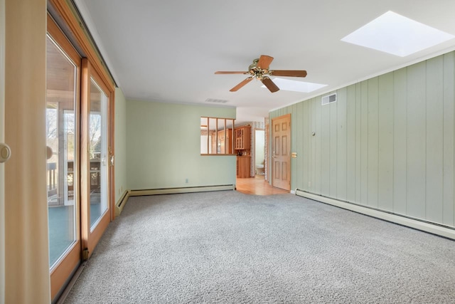 unfurnished living room featuring carpet flooring, a skylight, ceiling fan, a baseboard heating unit, and wood walls