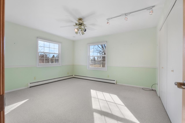 carpeted empty room featuring ceiling fan, track lighting, and a baseboard heating unit