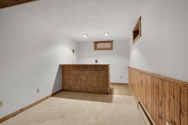 carpeted empty room with wooden walls and a baseboard radiator