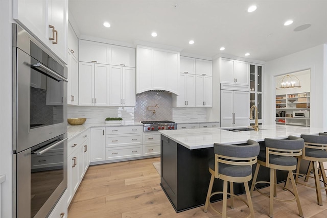 kitchen with light stone countertops, appliances with stainless steel finishes, sink, light hardwood / wood-style flooring, and white cabinetry