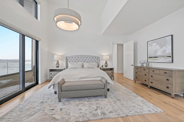 bedroom featuring access to exterior, a high ceiling, and light wood-type flooring