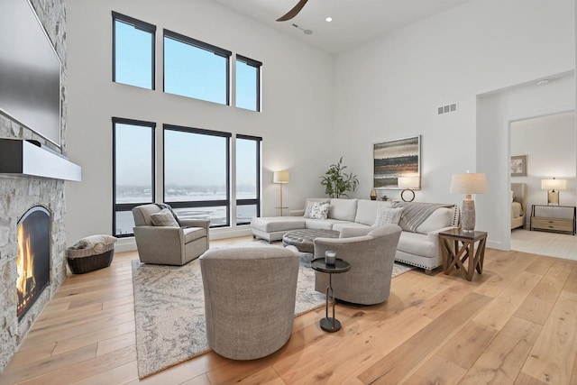 living room with ceiling fan, a high ceiling, a stone fireplace, light hardwood / wood-style flooring, and a water view