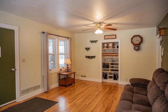 living room with ceiling fan, built in features, and light wood-type flooring