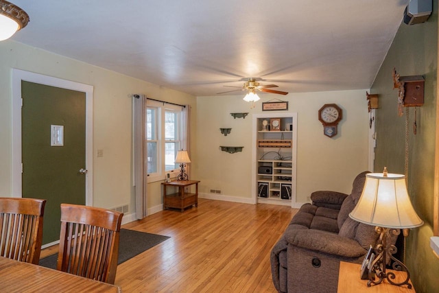 living room with built in shelves, light hardwood / wood-style flooring, and ceiling fan