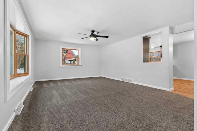 empty room featuring ceiling fan, dark carpet, and a wealth of natural light