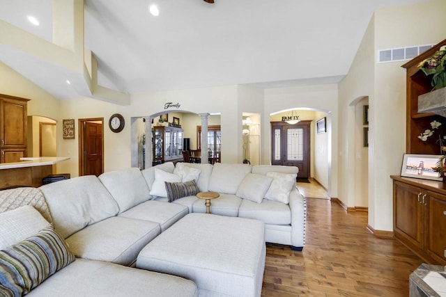 living room with light hardwood / wood-style floors, ornate columns, and high vaulted ceiling