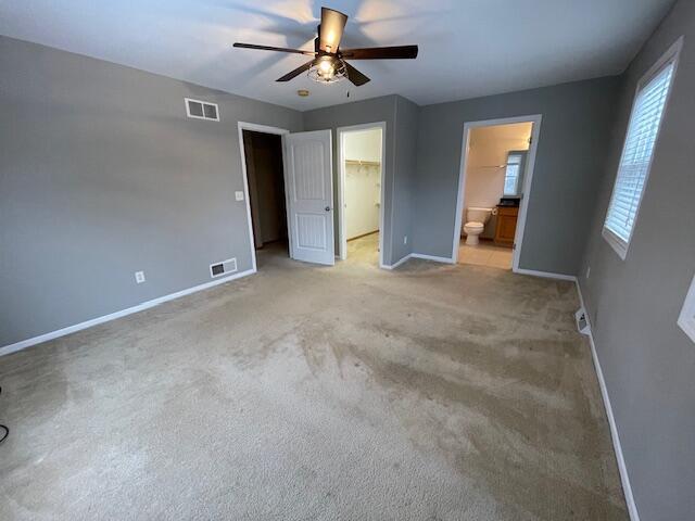 unfurnished bedroom featuring connected bathroom, ceiling fan, light colored carpet, a walk in closet, and a closet