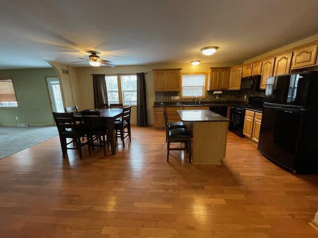 kitchen with a breakfast bar, ceiling fan, black appliances, light hardwood / wood-style flooring, and a kitchen island