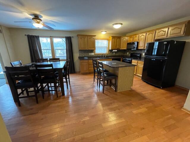 kitchen featuring a center island, black appliances, light hardwood / wood-style flooring, decorative backsplash, and a kitchen bar