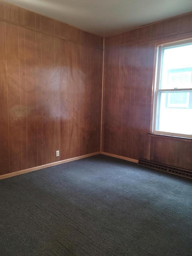 carpeted empty room with wood walls and a baseboard radiator