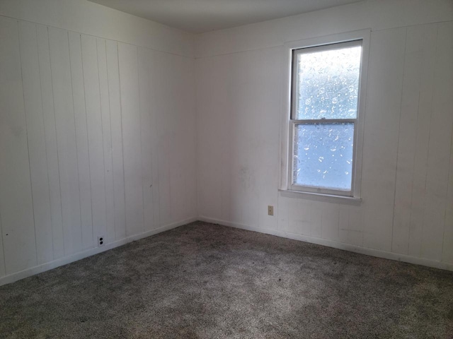 spare room featuring dark colored carpet and wood walls