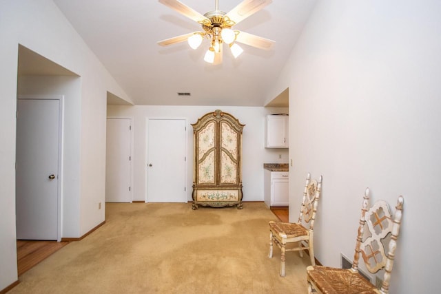 living area featuring ceiling fan, light carpet, and vaulted ceiling