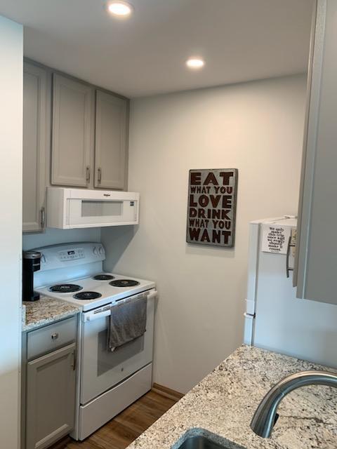 kitchen featuring dark hardwood / wood-style floors, gray cabinets, light stone counters, and white appliances