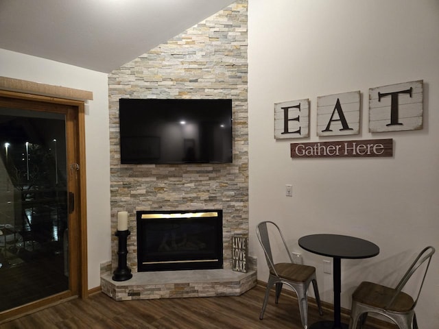 living room featuring hardwood / wood-style flooring, a stone fireplace, and vaulted ceiling