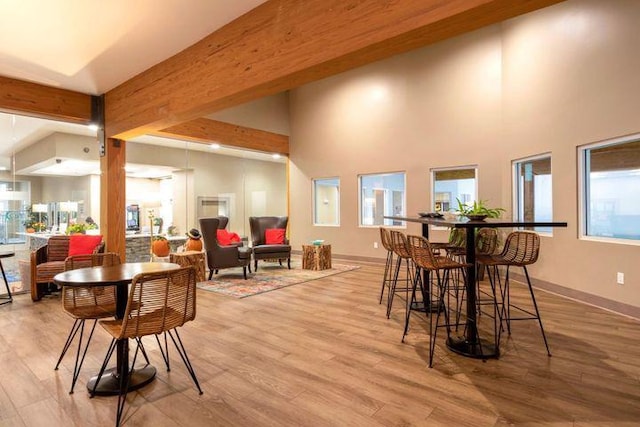 dining area featuring beam ceiling, light wood-type flooring, and a high ceiling