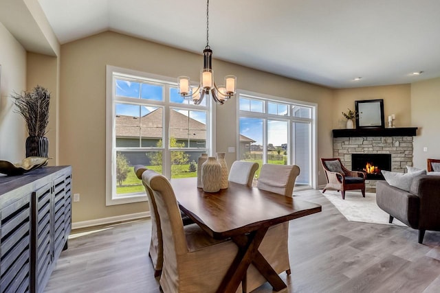 dining area featuring light hardwood / wood-style floors, a stone fireplace, and a notable chandelier