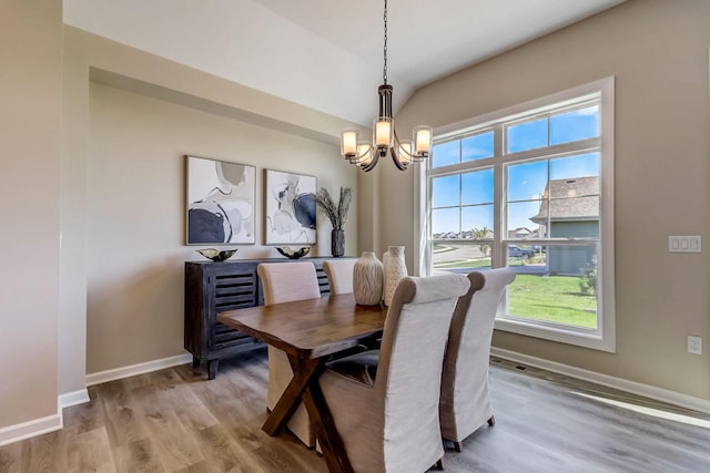 dining space with hardwood / wood-style flooring, lofted ceiling, and a chandelier