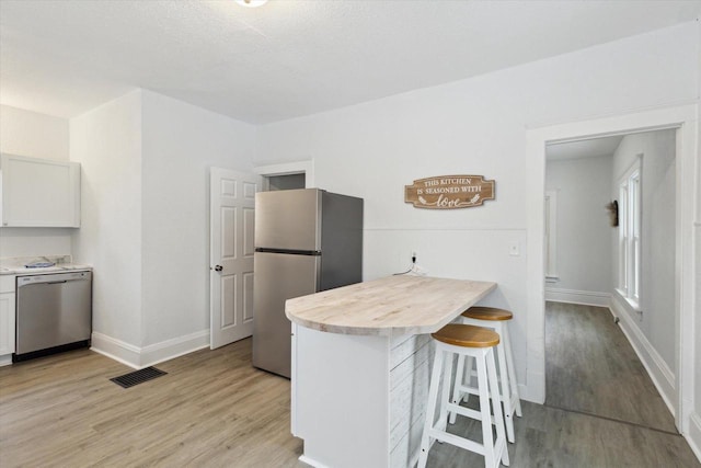 kitchen with white cabinets, light wood-type flooring, appliances with stainless steel finishes, a kitchen bar, and kitchen peninsula