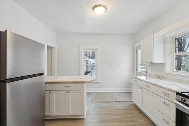 kitchen featuring stove, white cabinetry, stainless steel refrigerator, and a healthy amount of sunlight