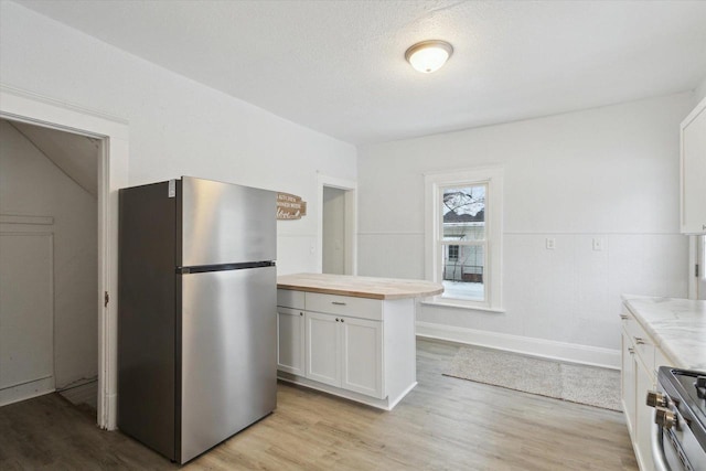 kitchen featuring wood counters, a textured ceiling, light hardwood / wood-style floors, white cabinetry, and stainless steel appliances