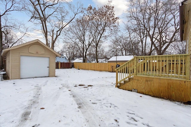 yard layered in snow with an outbuilding, a deck, and a garage