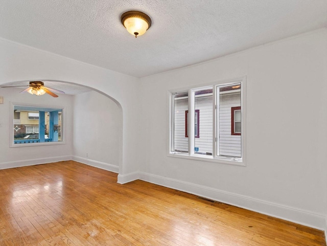 empty room featuring ceiling fan, light hardwood / wood-style floors, a textured ceiling, and a wealth of natural light