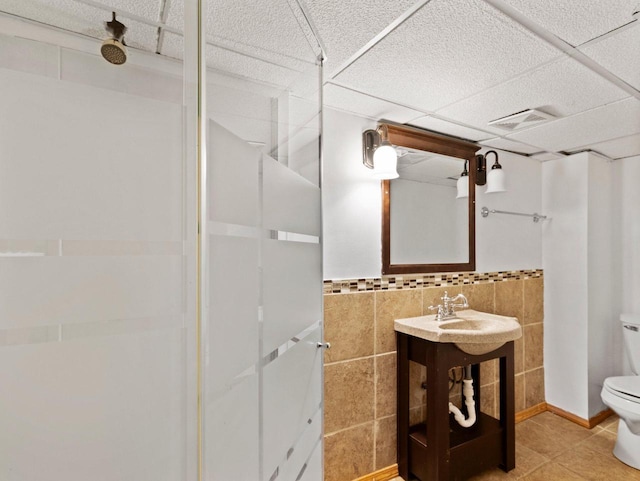 bathroom with a shower, a drop ceiling, tile walls, and toilet