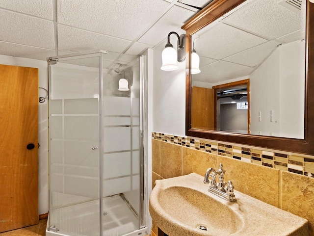 bathroom featuring decorative backsplash, sink, a drop ceiling, and walk in shower